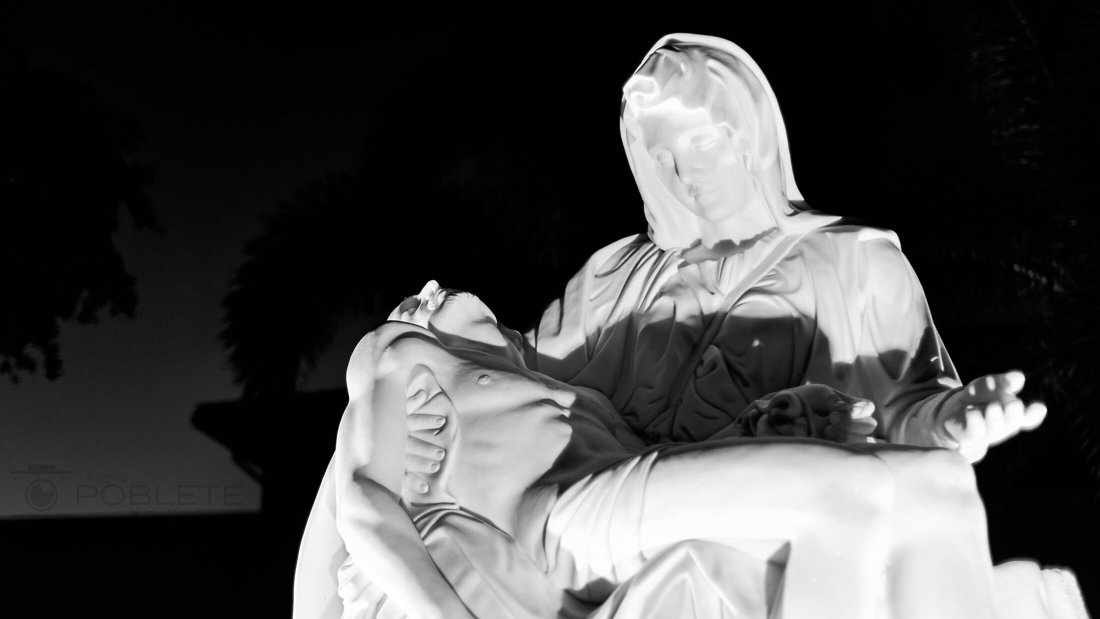 A pale sculpture of a seated figure holding a reclining body.