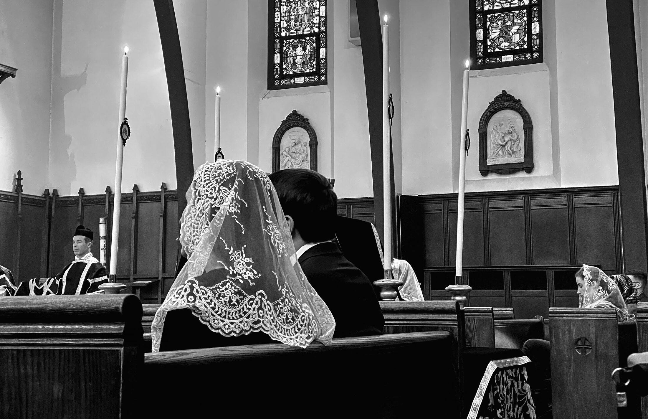 A woman wearing a lace veil sits in a church pew.