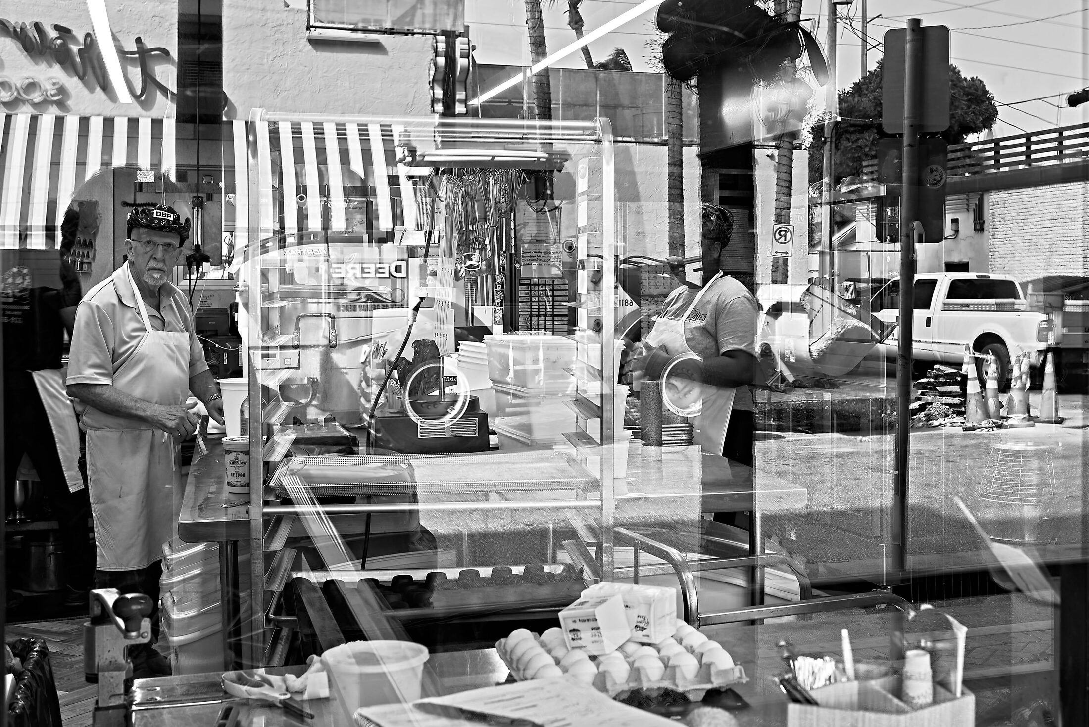 A shop worker is seen through a window layered with street reflections.