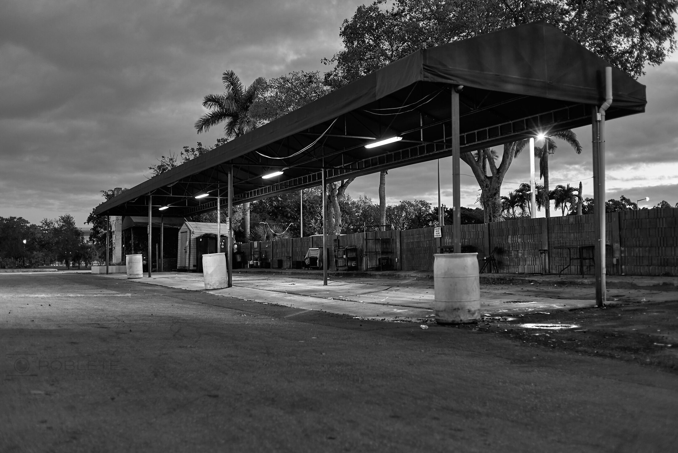 An empty roadside produce stand sits beneath a long metal roof.