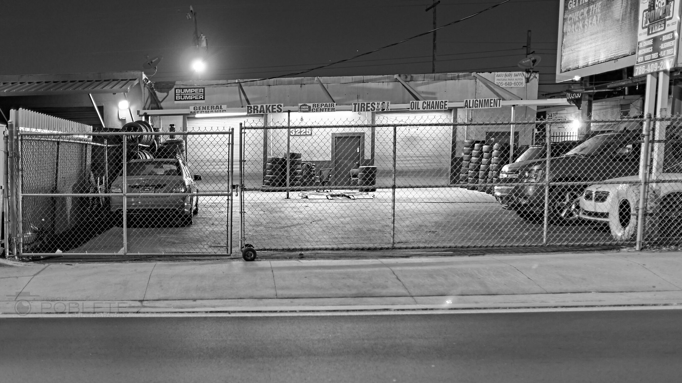 An empty tire repair garage is seen through a chain-link fence at dawn.