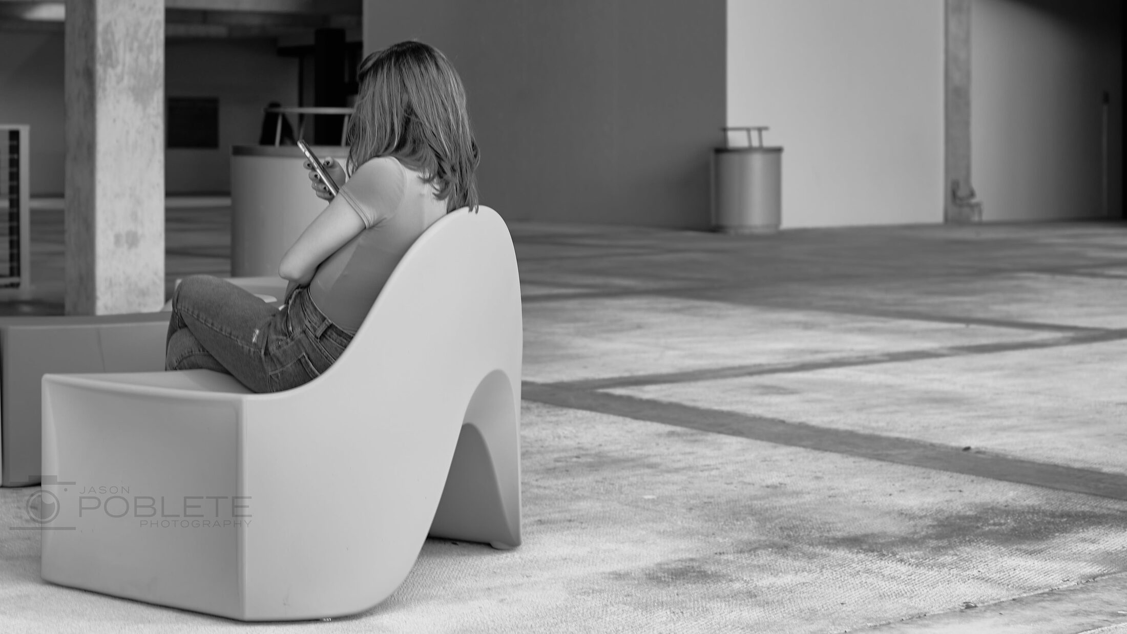 A solitary person sits on a sculptural bench in an open courtyard.