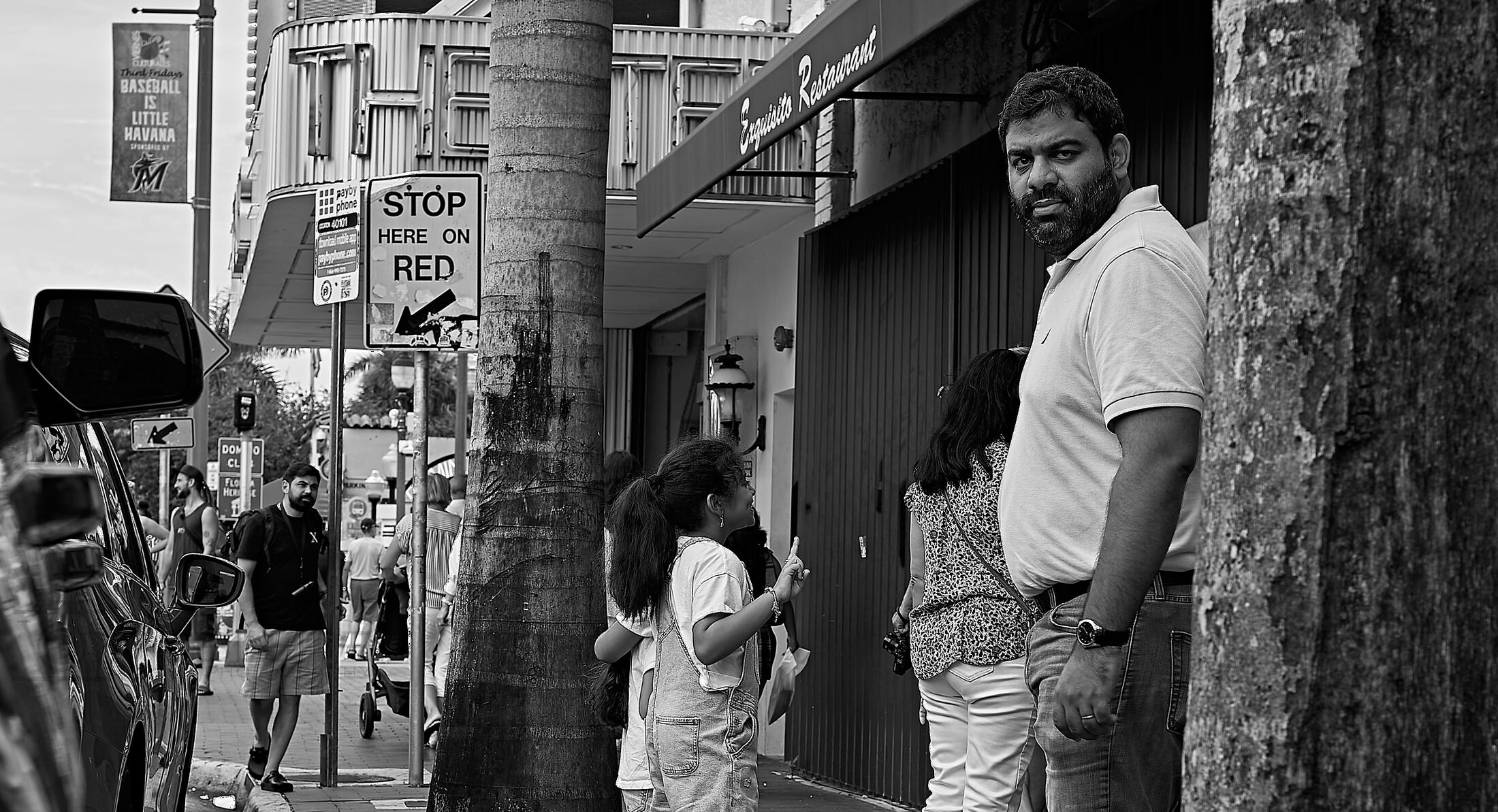Pedestrians pass a display of posters and artwork along a busy sidewalk.