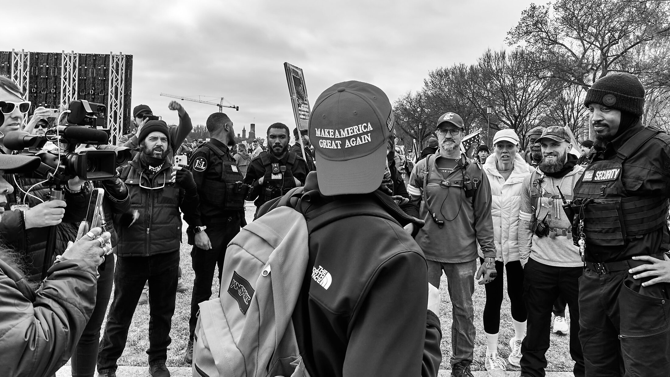 A dense crowd gathers outdoors, with one person turning toward the camera.