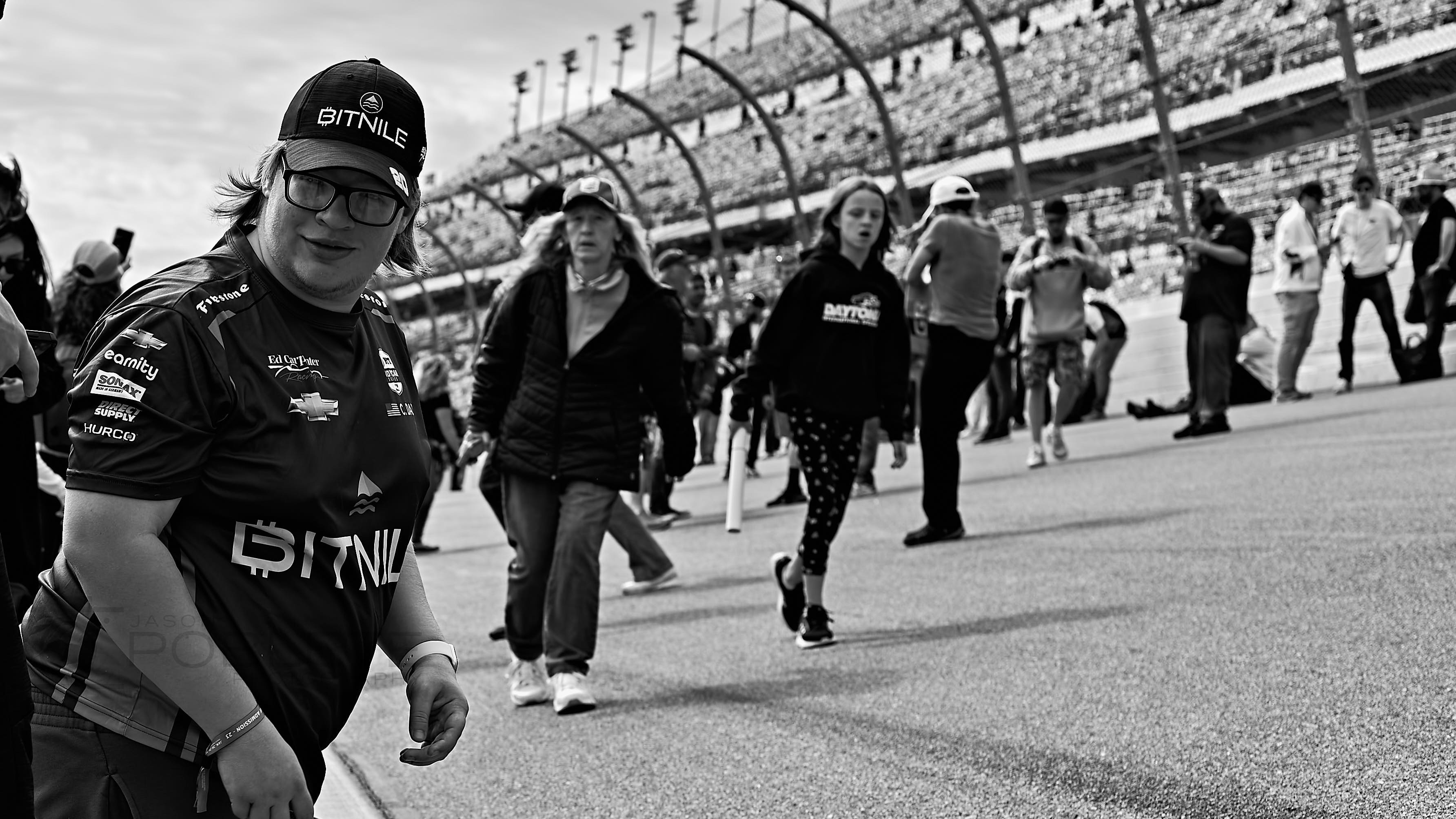 A race fan walks through a crowd at a motor speedway.