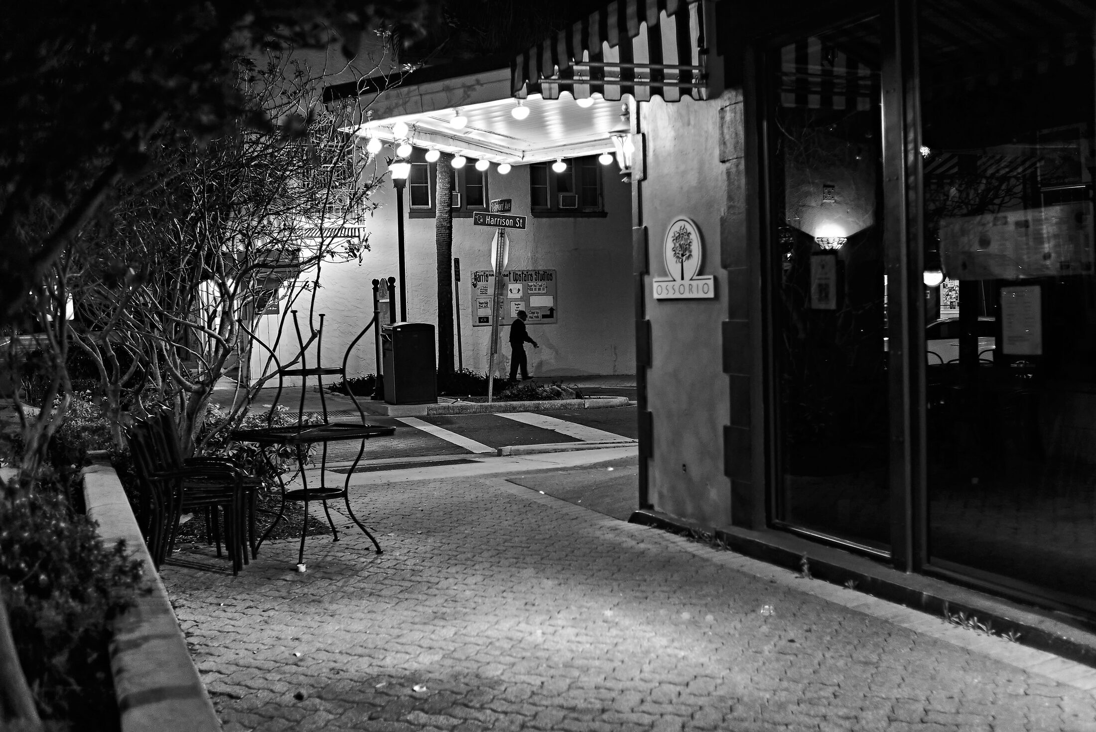 A solitary figure walks through a pool of light on a narrow street.