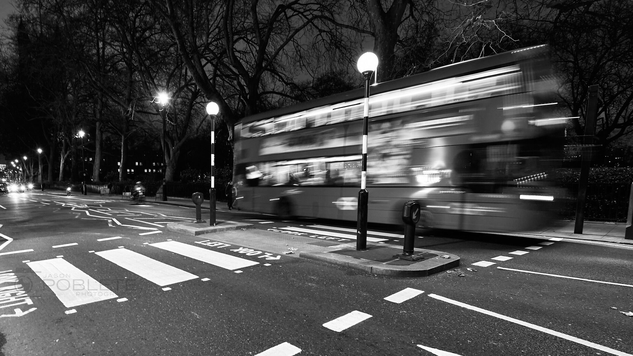 A city bus blurs across a striped crosswalk at night.