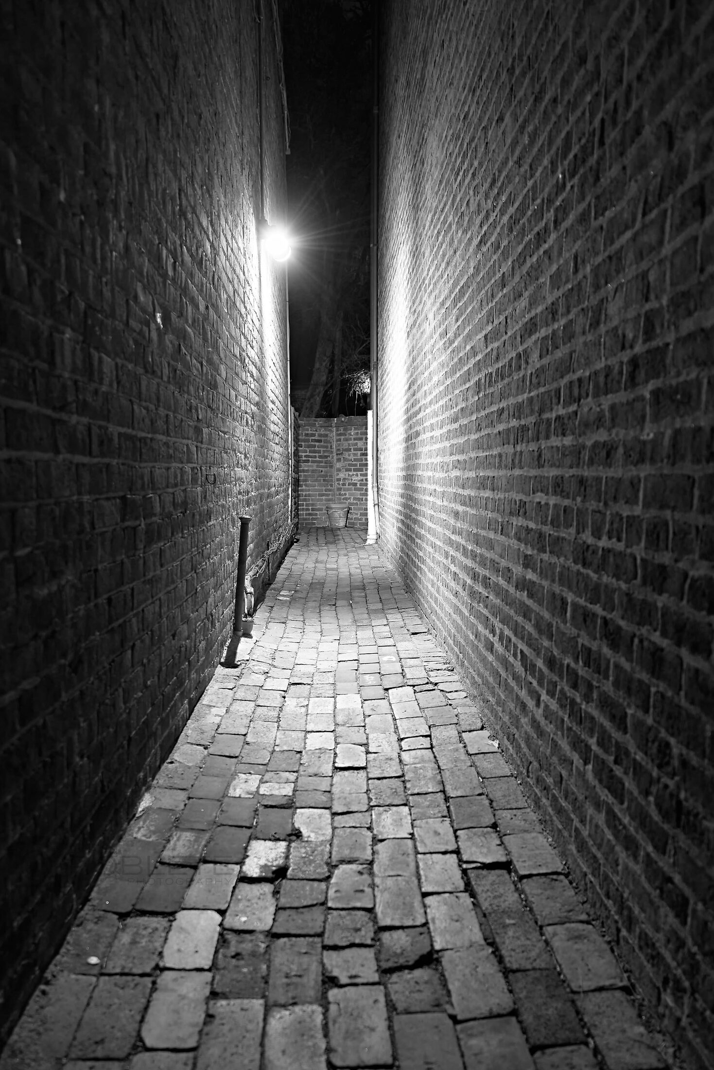 A narrow brick passage leads toward a bright wall-mounted light.