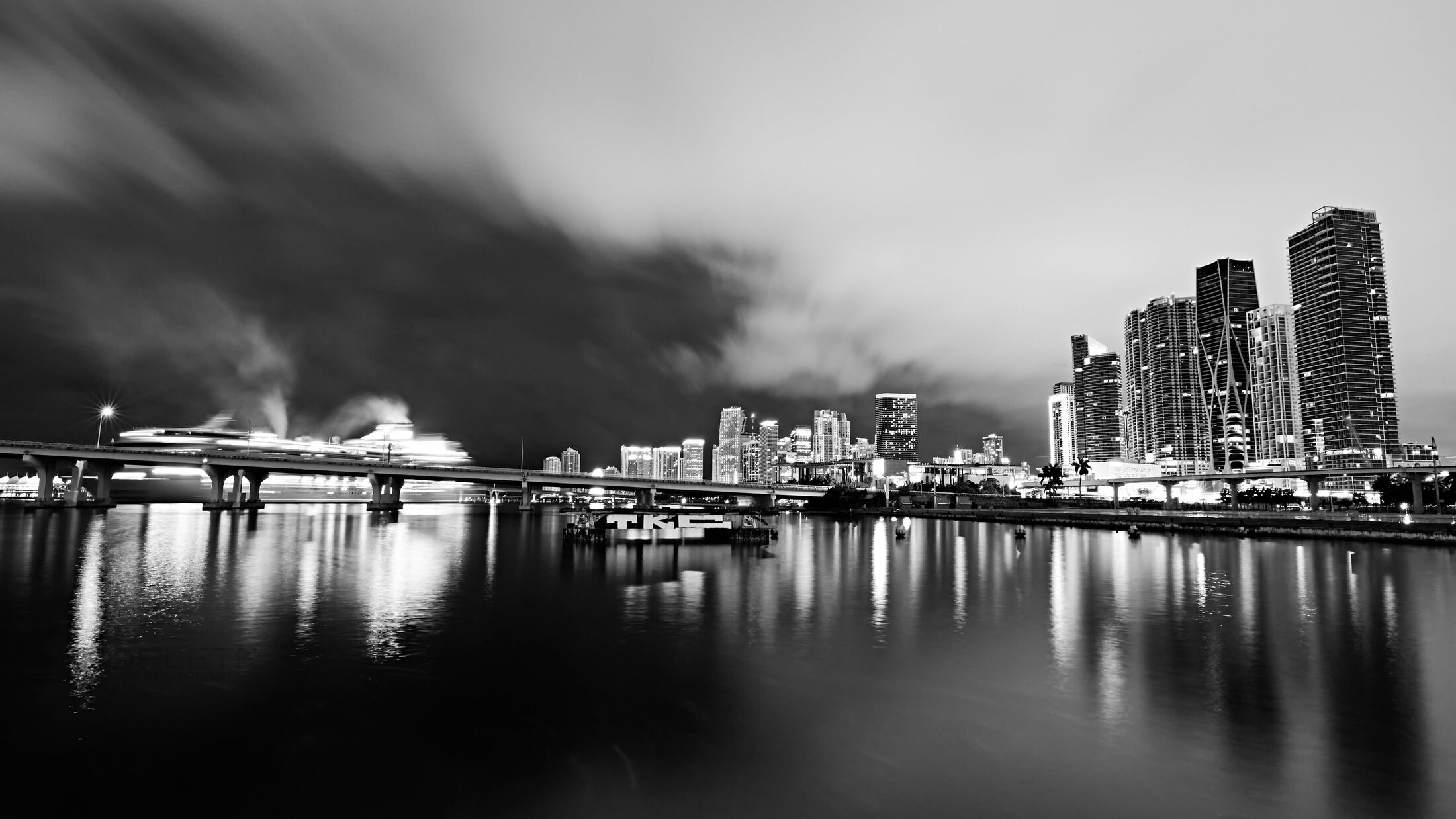 A luminous city skyline is reflected across still water at night.
