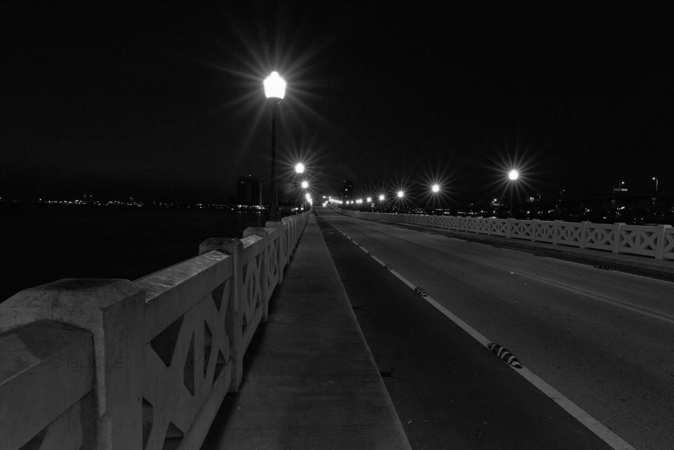 Streetlights recede along an empty bridge at night.
