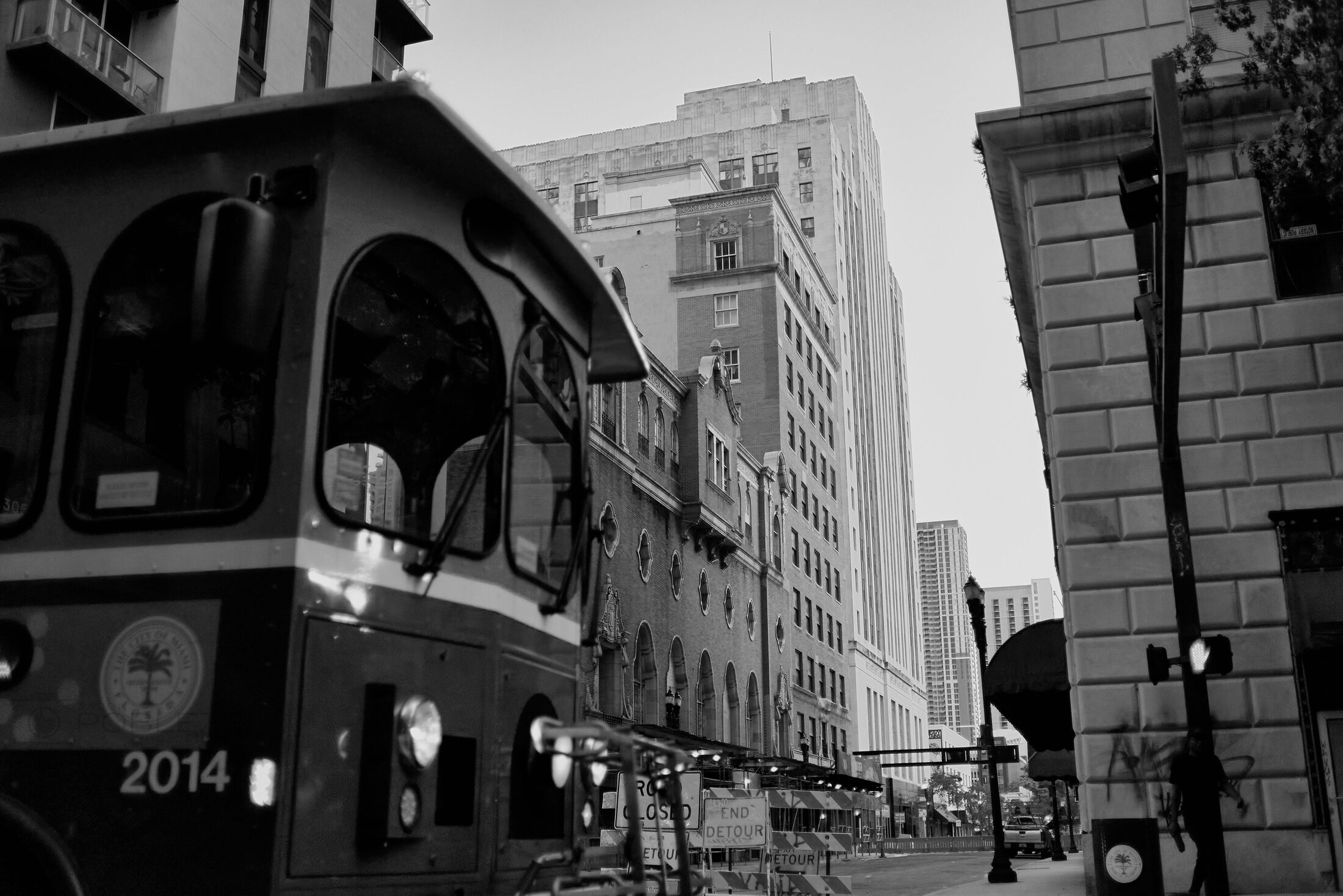 A person crosses a downtown street between tall buildings.