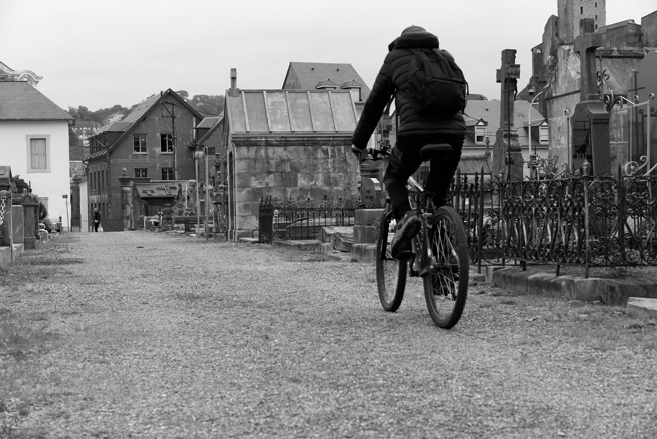 A cyclist rides past a cemetery bordered by old buildings.