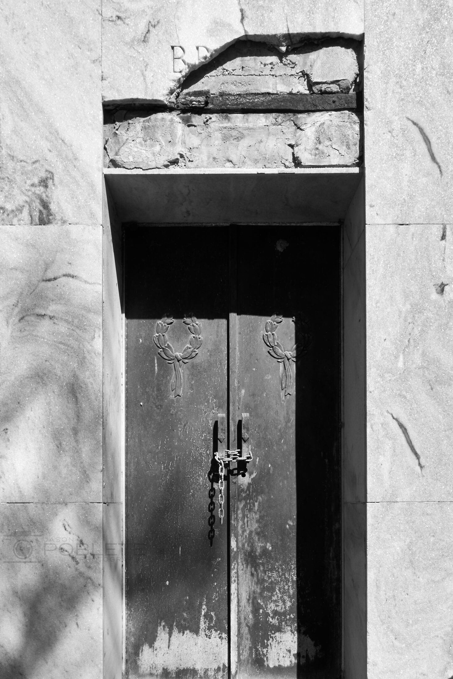 A closed metal door is set into a pale stone mausoleum.