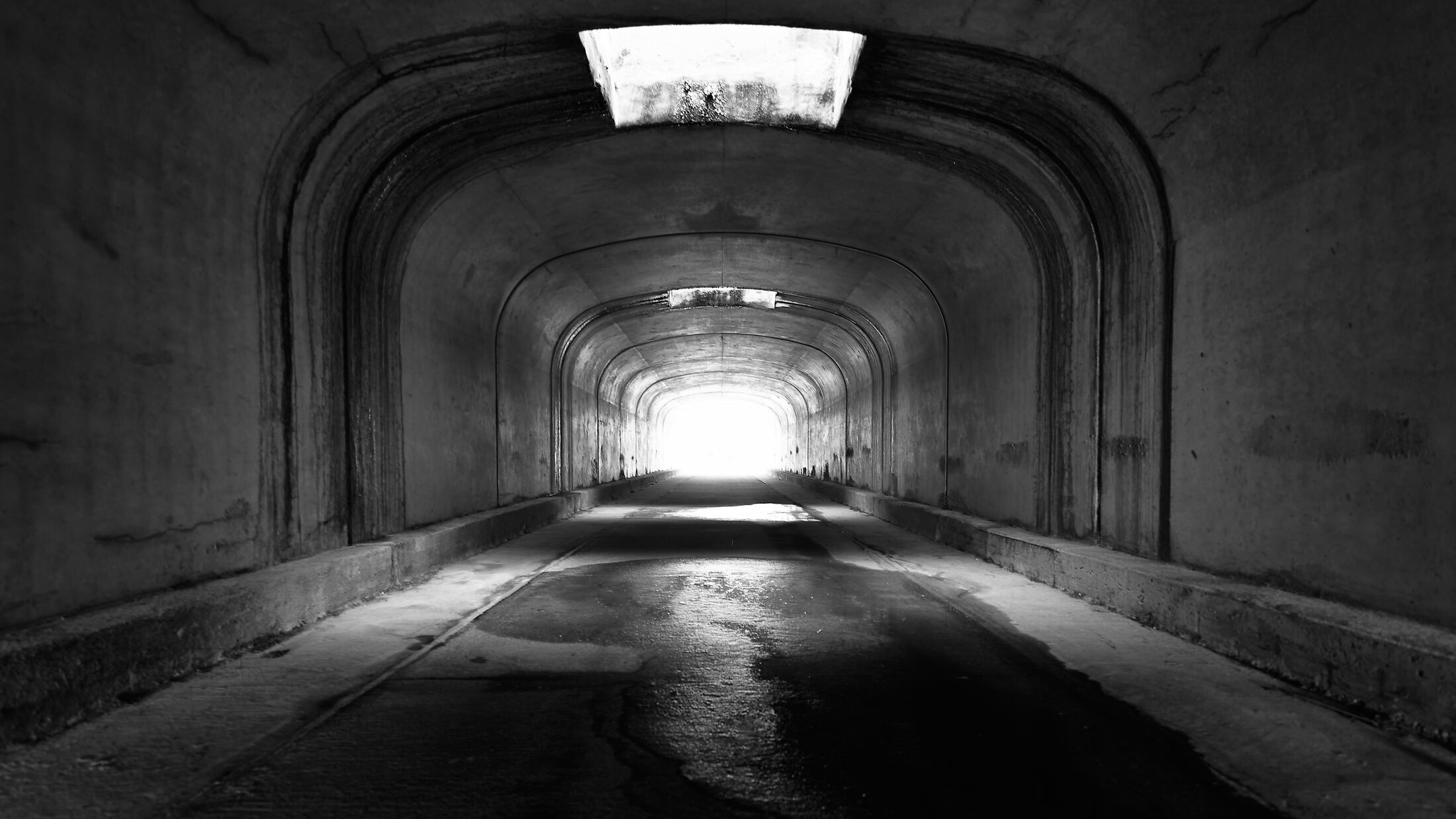 Light glows at the far end of an empty arched mausoleum corridor.