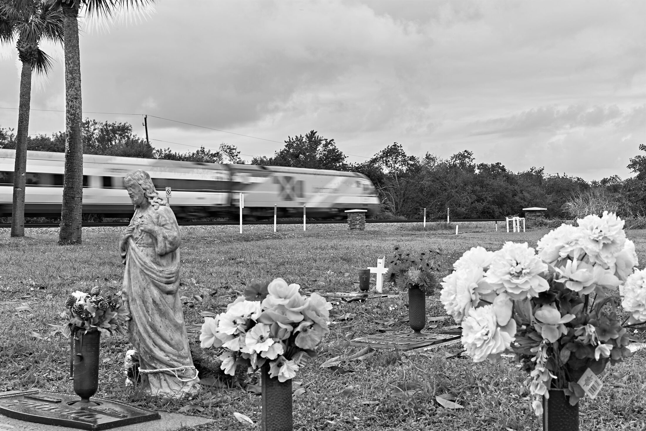 A visitor stands beside flower-covered graves in a cemetery.