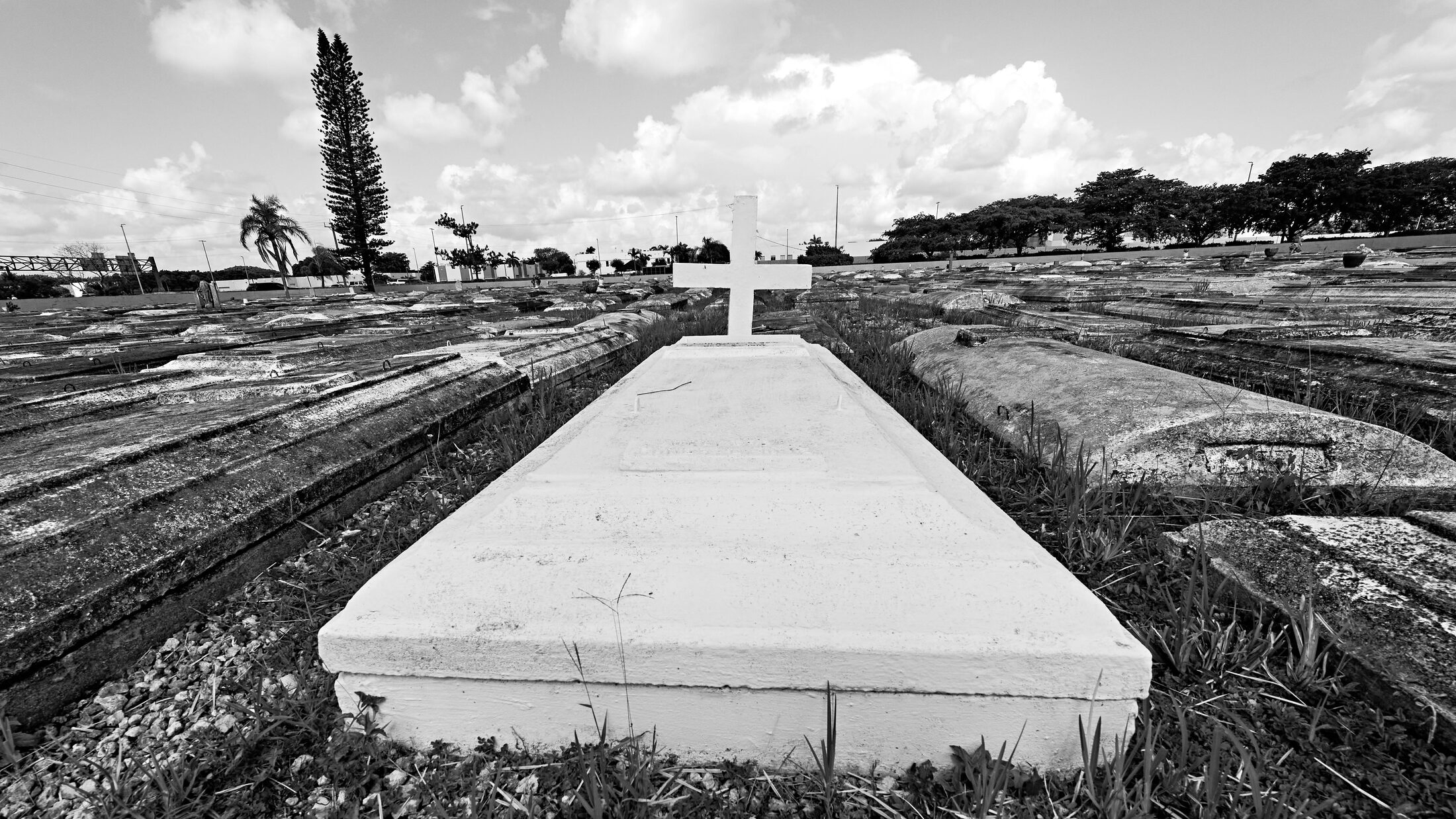 A white grave and cross stand among rows of weathered burial slabs.