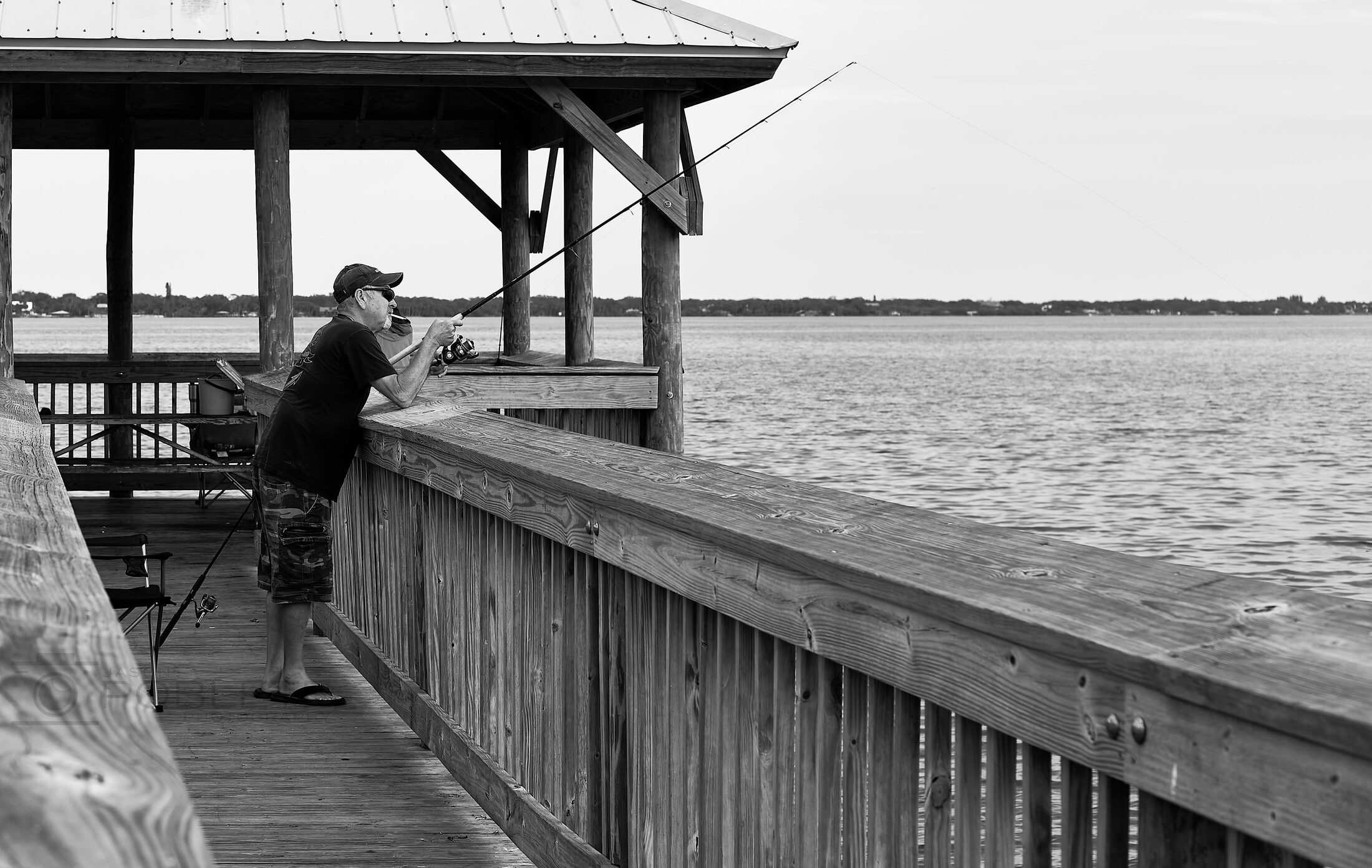 A person looks over the water from inside a wooden pier shelter.